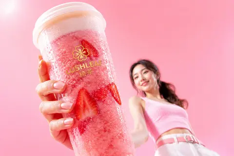 一张高质感商业饮品广告摄影，低机位仰拍、超广角近景透视夸张构图，前景是一只被手高高举起的超大杯粉红色草莓冰沙奶盖饮品，透明塑料杯、白色杯盖，杯身布满细密冷凝水珠 - AI生成图片 2